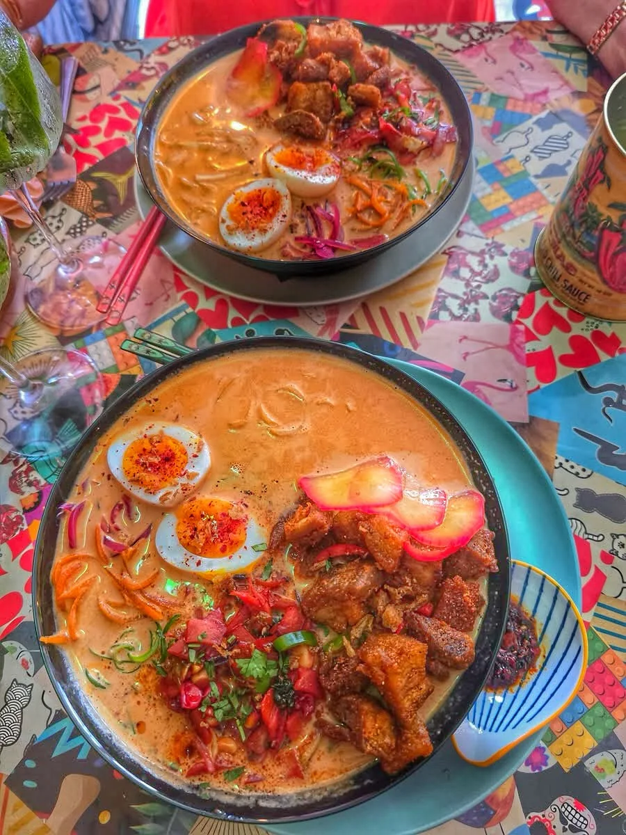 Two richly sauced bowls served on a colourful table